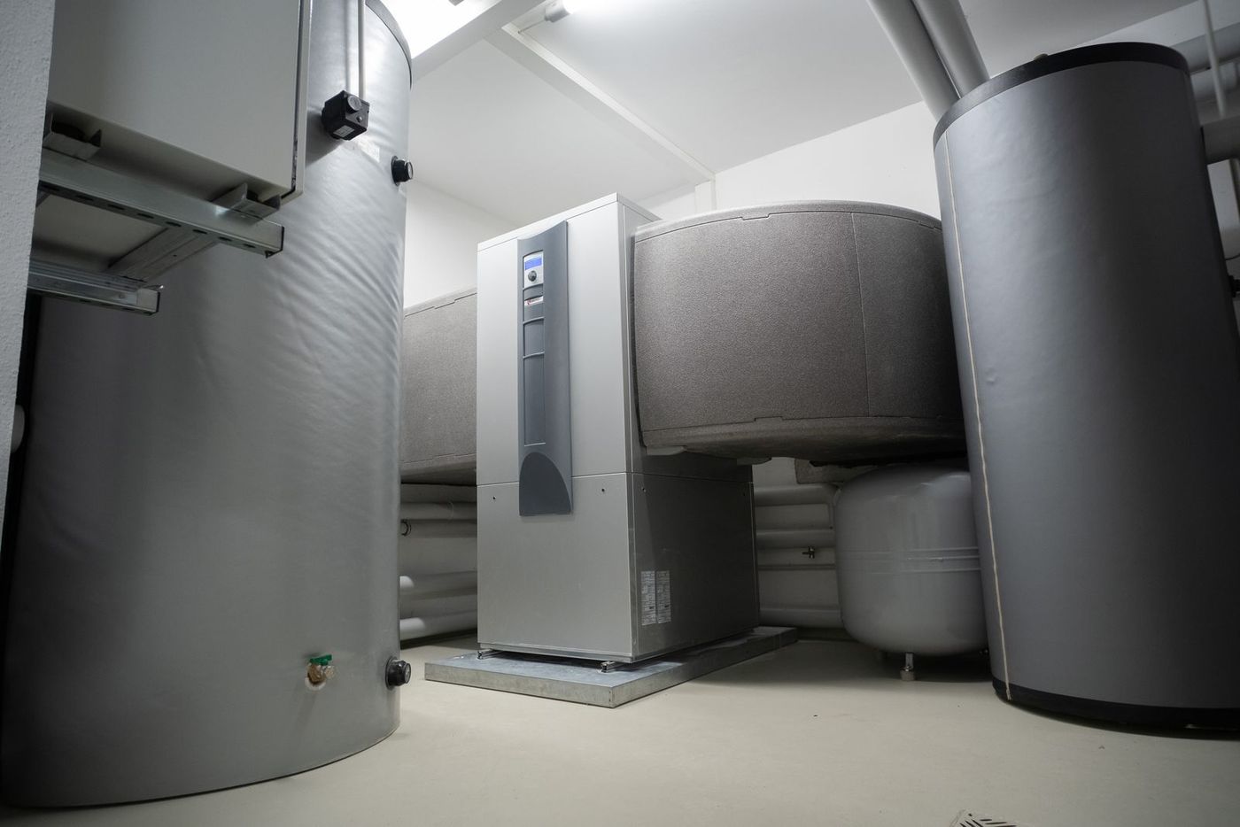An indoor heat pump unit alongside insulated buffer and hot water cylinders in a plant room